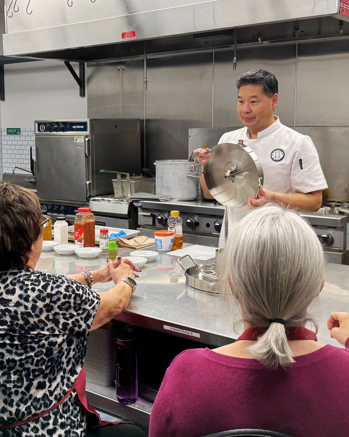 UpRoaster instructor demonstrating the vertical roasting pan and attachments to students during a DIY Peking Duck cooking class in a commercial kitchen